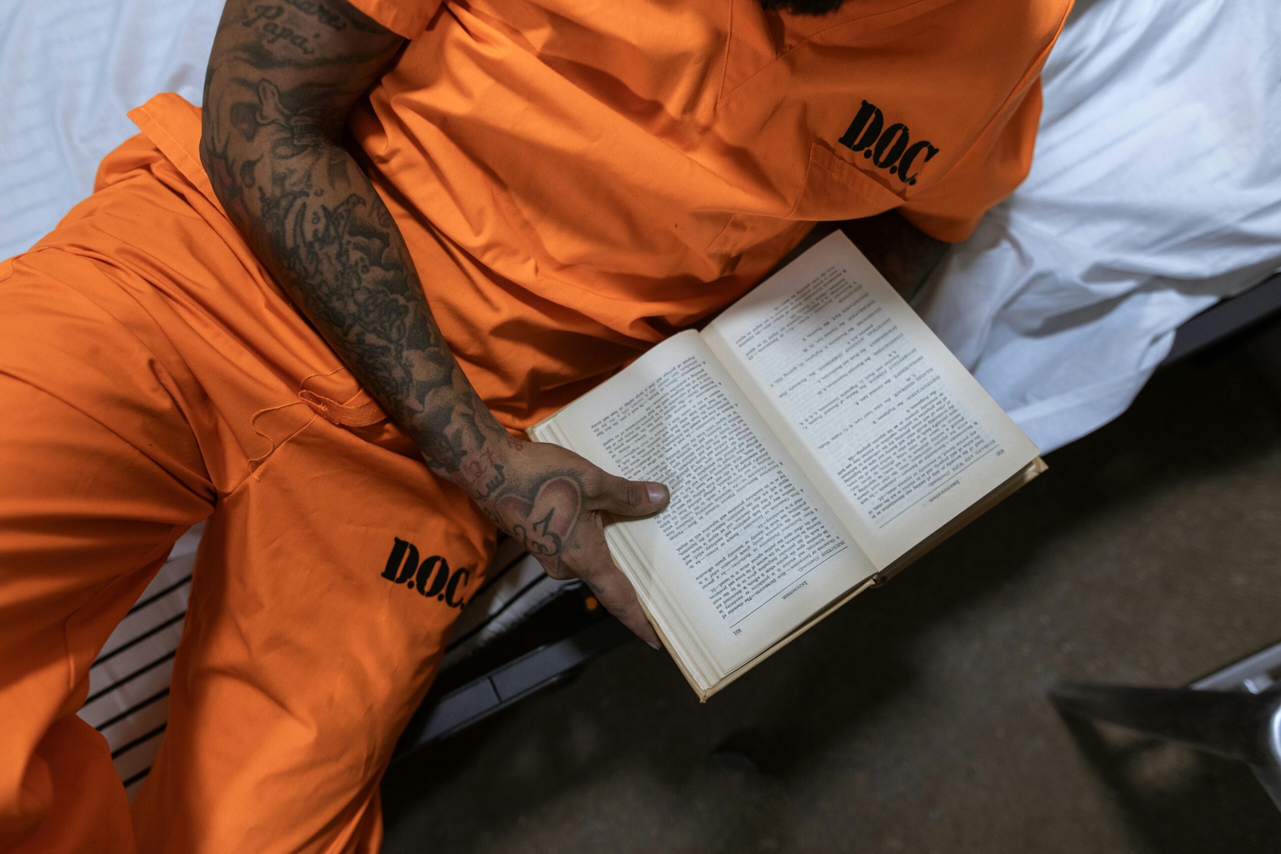 person in orange prison outfit reading book on bed