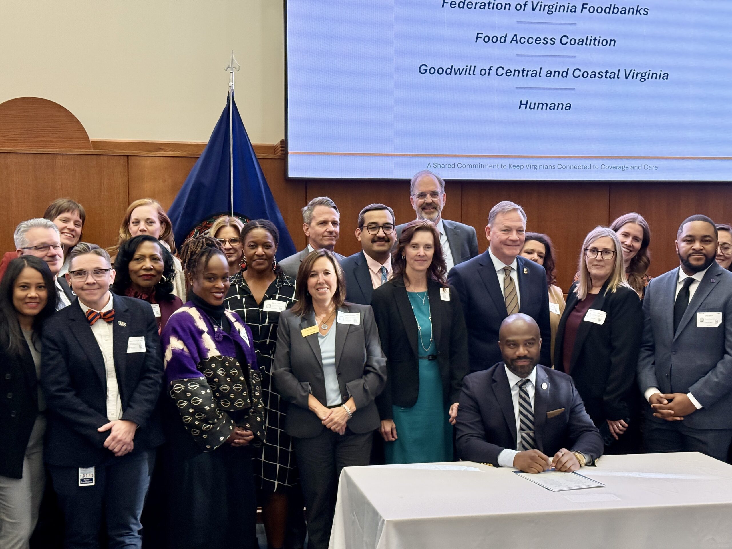 man signing document with many people standing behind him